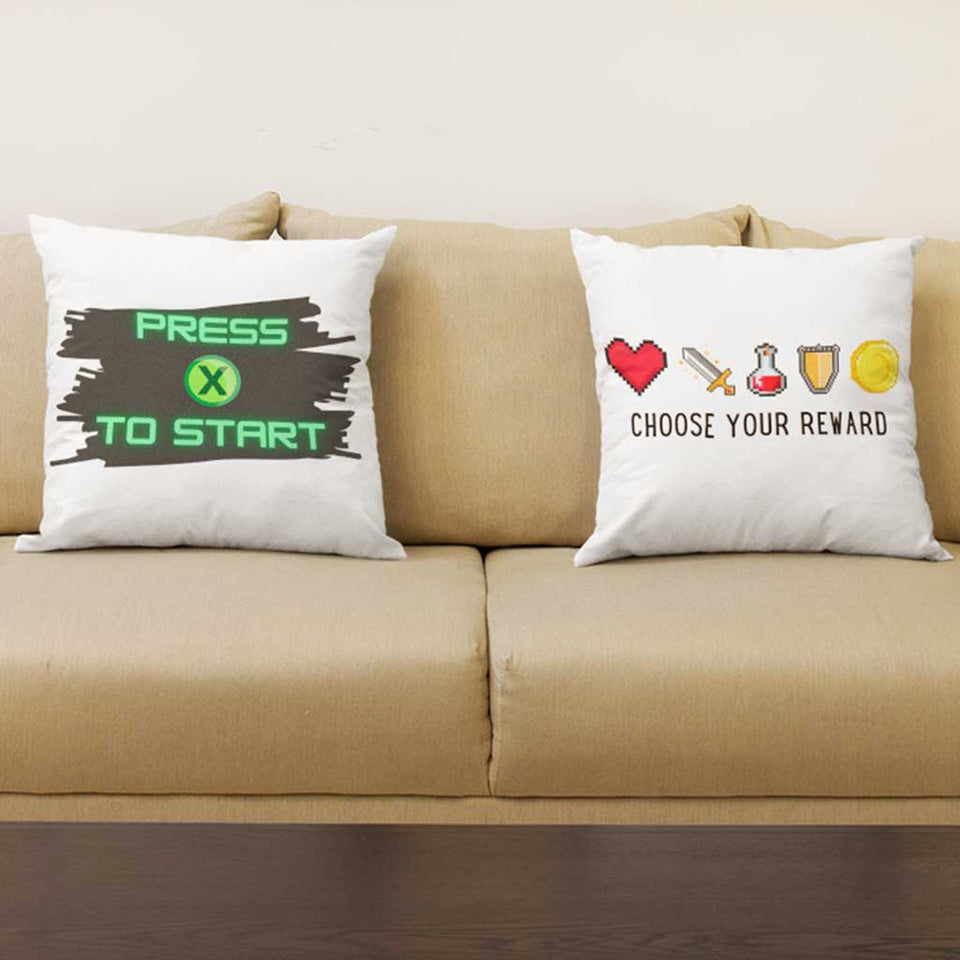 Two gamer related pillows on a gamer couch.  One pillow with Press X to Start for console gamers and one Choose Your Reward video game related design. 
